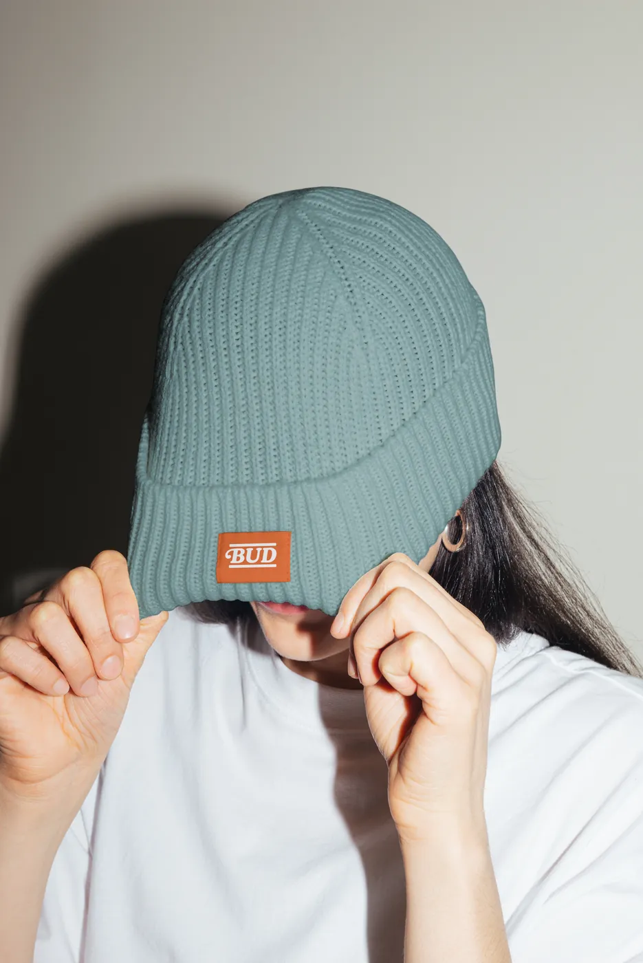 Pessoa puxando o gorro com a etiqueta Bud sobre os olhos